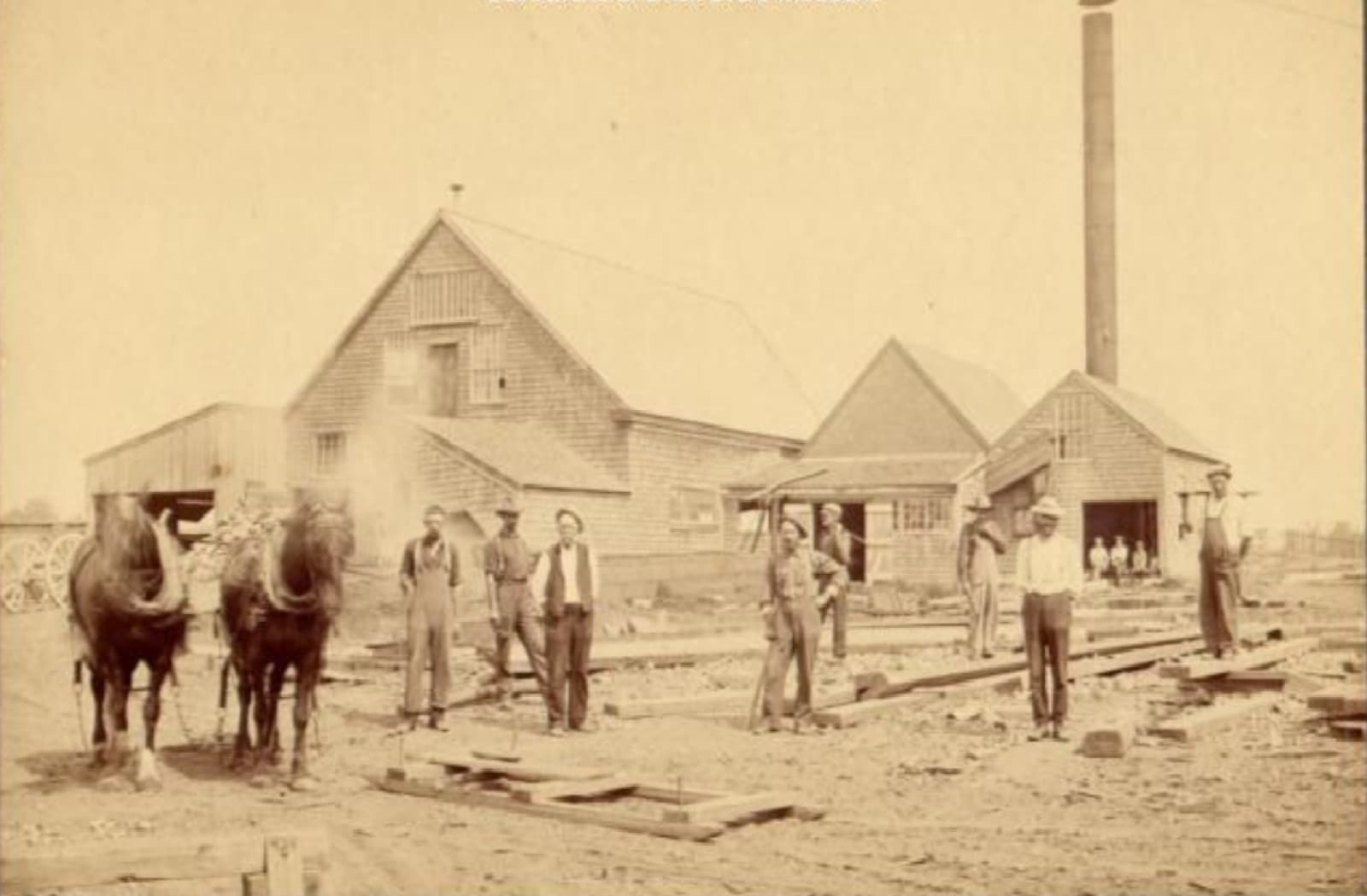 The Clark shipyard in the 1800s, workers and draft horses outside the sheds.