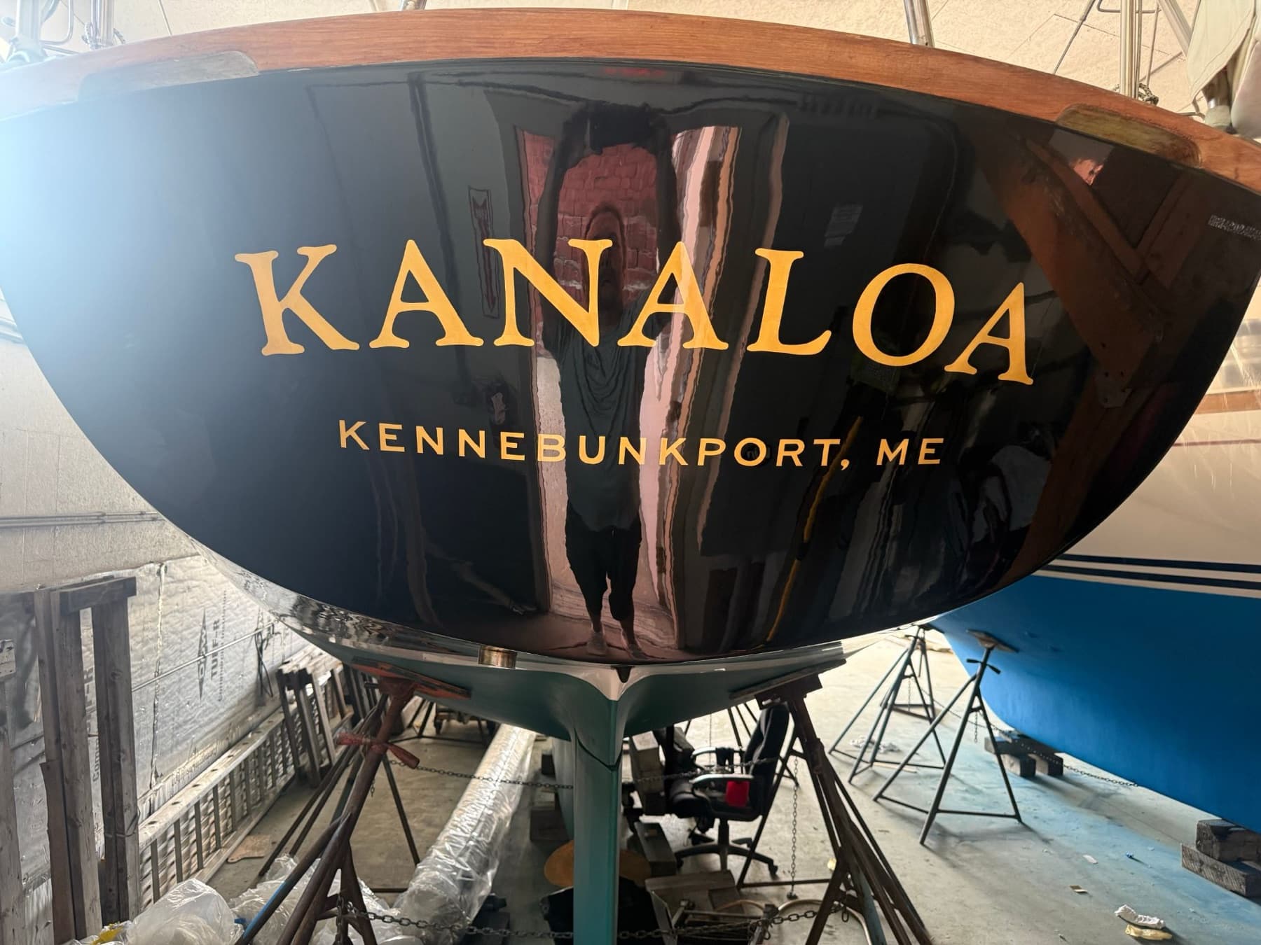 Glossy black transom reading KANALOA, Kennebunkport ME, in gold-leaf lettering, with varnished wood cap rail.
